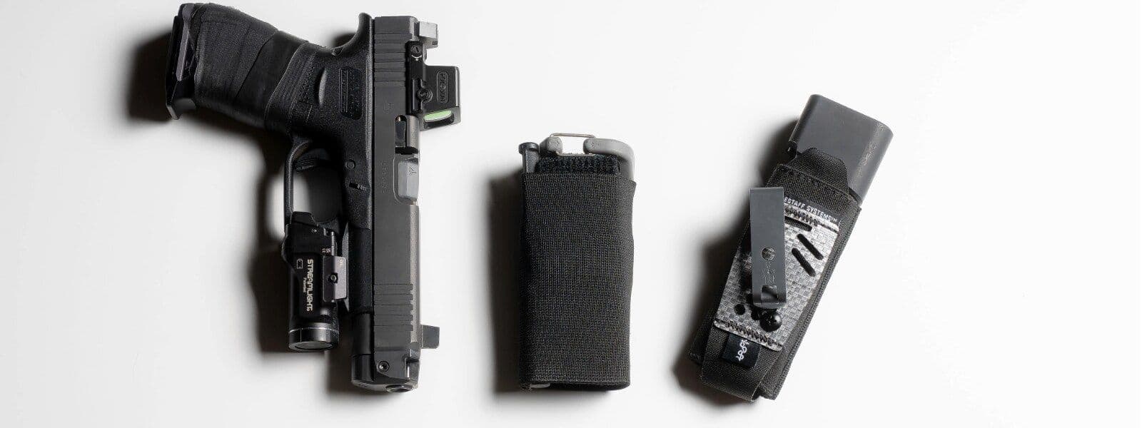 An everyday-carry layout seen from above: a pistol with a weapon light, a spare magazine, and an ETQ in a Snakeskin sleeve — the tourniquet no bulkier than the magazine beside it.